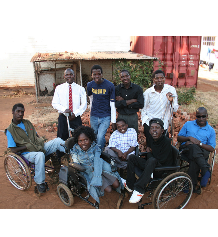 A group of eight black men and a black women. The five people in the front are sitting in a wheelchair. The four people in the back are standing, the one on the right holding crutches.
