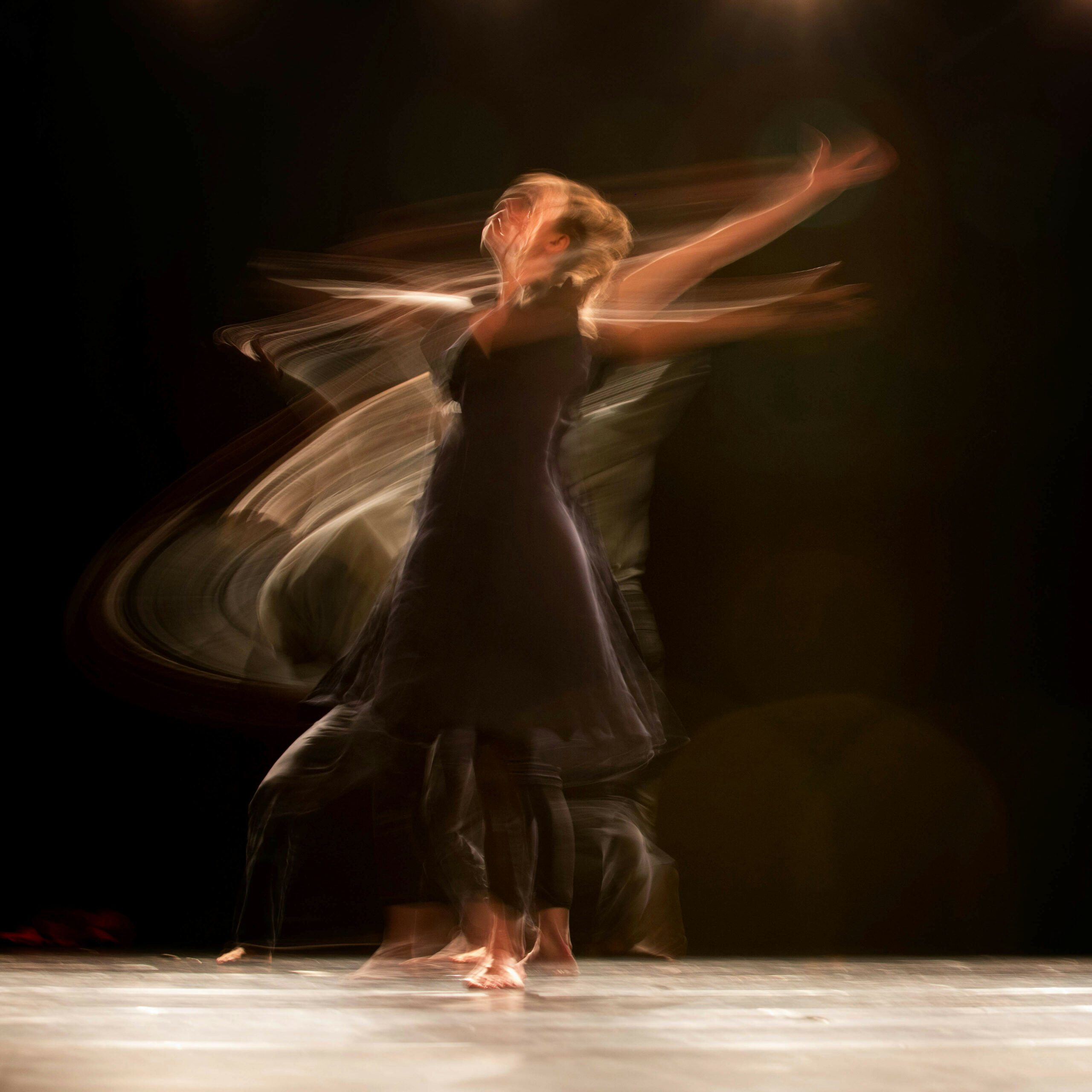 A dancer on stage, bare feet, wearing a black outfit, turning very fast.