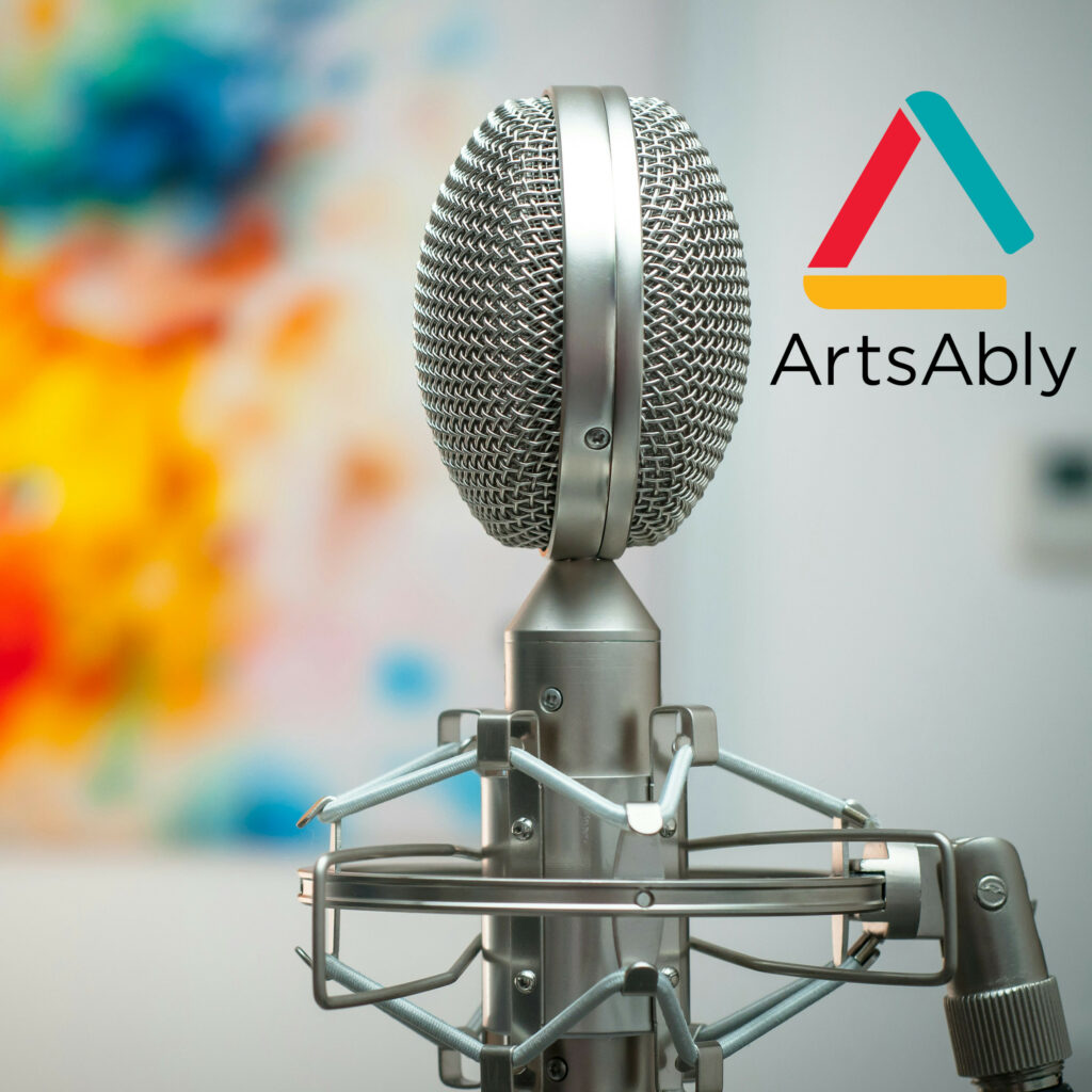 A microphone in the centre of the picture, and the logo of ArtsAbly on the right. The background is blurry with multiple colour spots.