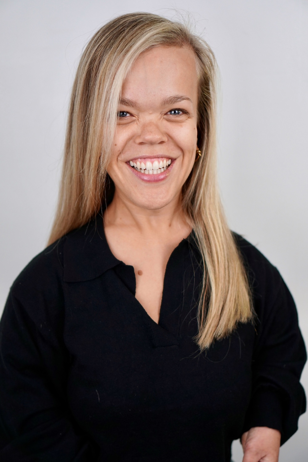 A white woman with long blond hair wearing a black top, smiles at the camera.