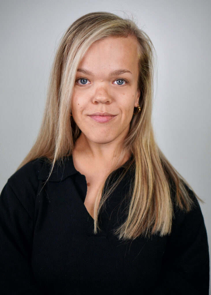 A white woman with long blond hair wearing a black top.