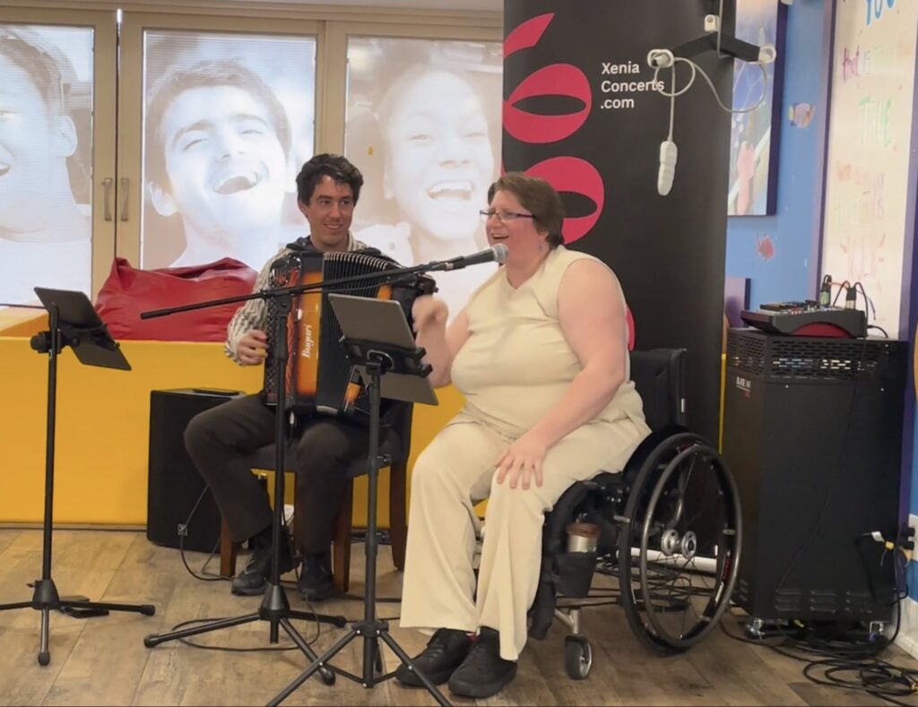 Michael Bridge and his accordion, and Diane Kolin in front of a microphone, in a concert in Safehaven.