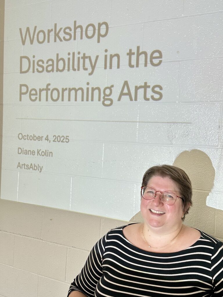 Slide projected on a wall, it reads: Disability in the Performing Arts, October 4, 2025, Diane Kolin, ArtsAbly. On the bottom right corner, Diane's head, a white woman with short brown hair and red glasses.