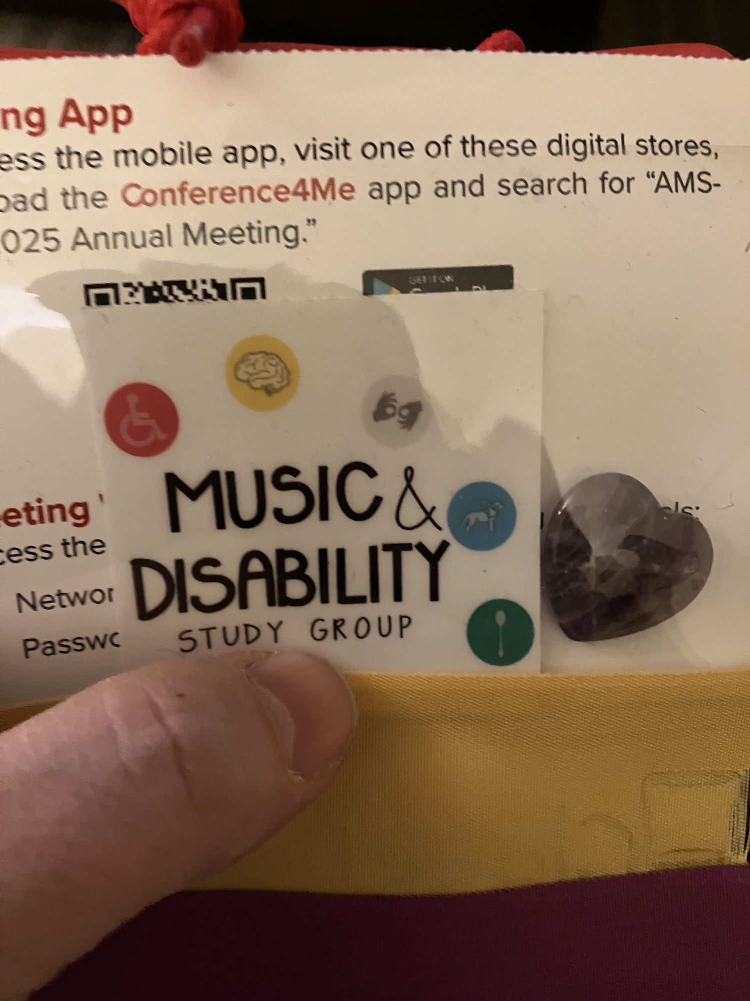 A sticker that says Music and Disability Study Group with logos representing a wheelchair, a brain, hands signing, a dog and a spoon. On the right, a small dark blue stone in the shape of a heart.