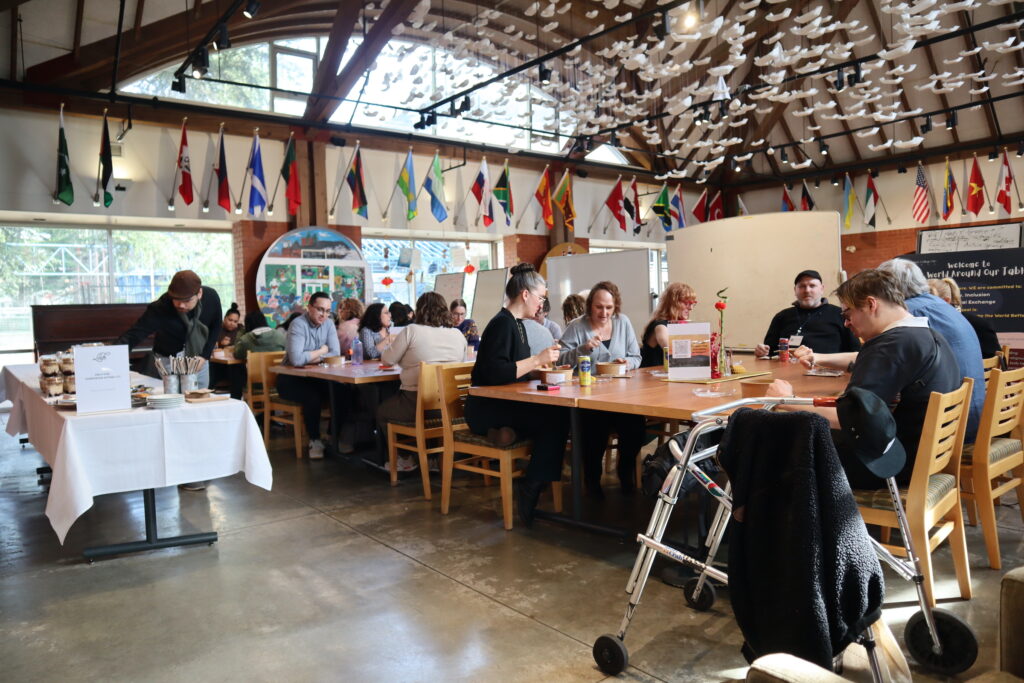 People having lunch in a large hall with flags all around the room and an art installation with folded boats on the ceiling.