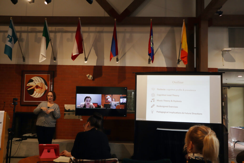 A white woman presenting remotely, her presentation about dyslexia is projected on the larger screen on the right.
