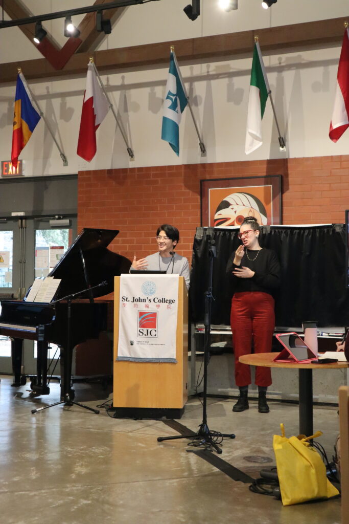 An Asian man wearing a grey shirt presents at the wooden stand.