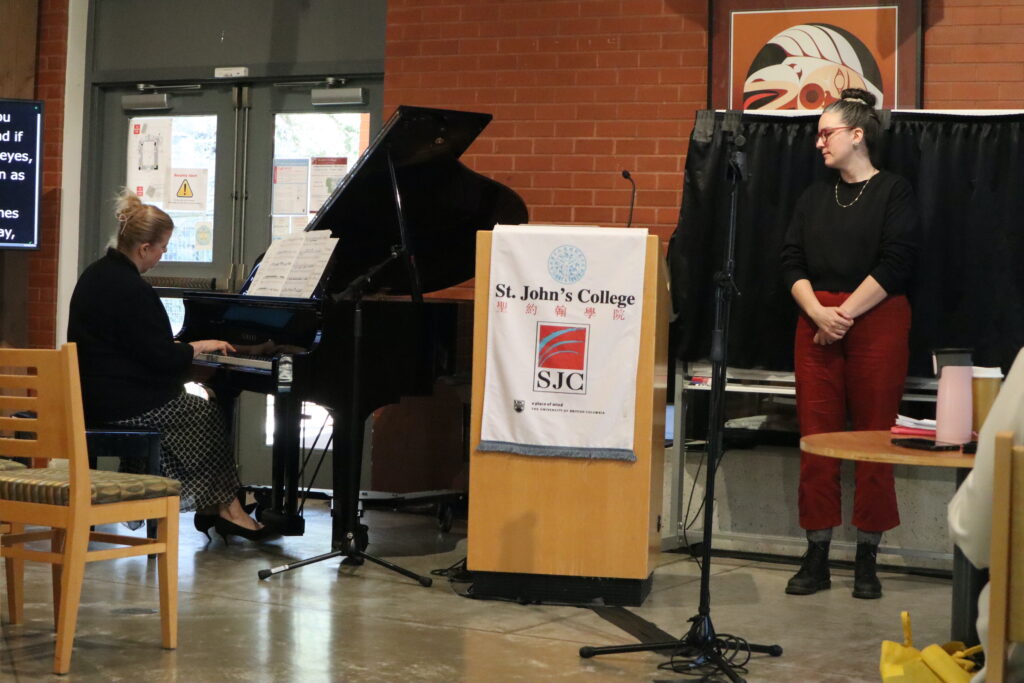 A white woman with blond hair and wearing a black top and a black and white skirt plays the piano.