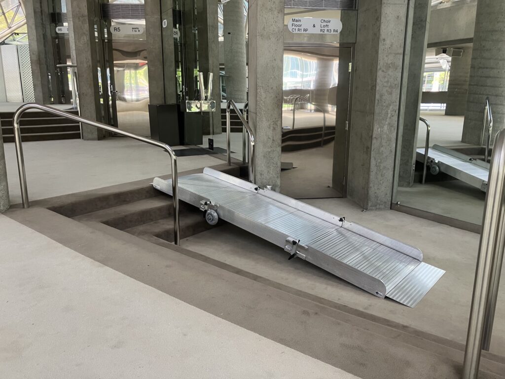A grey metallic ramp above three steps in a performing venue with lots of mirrors.